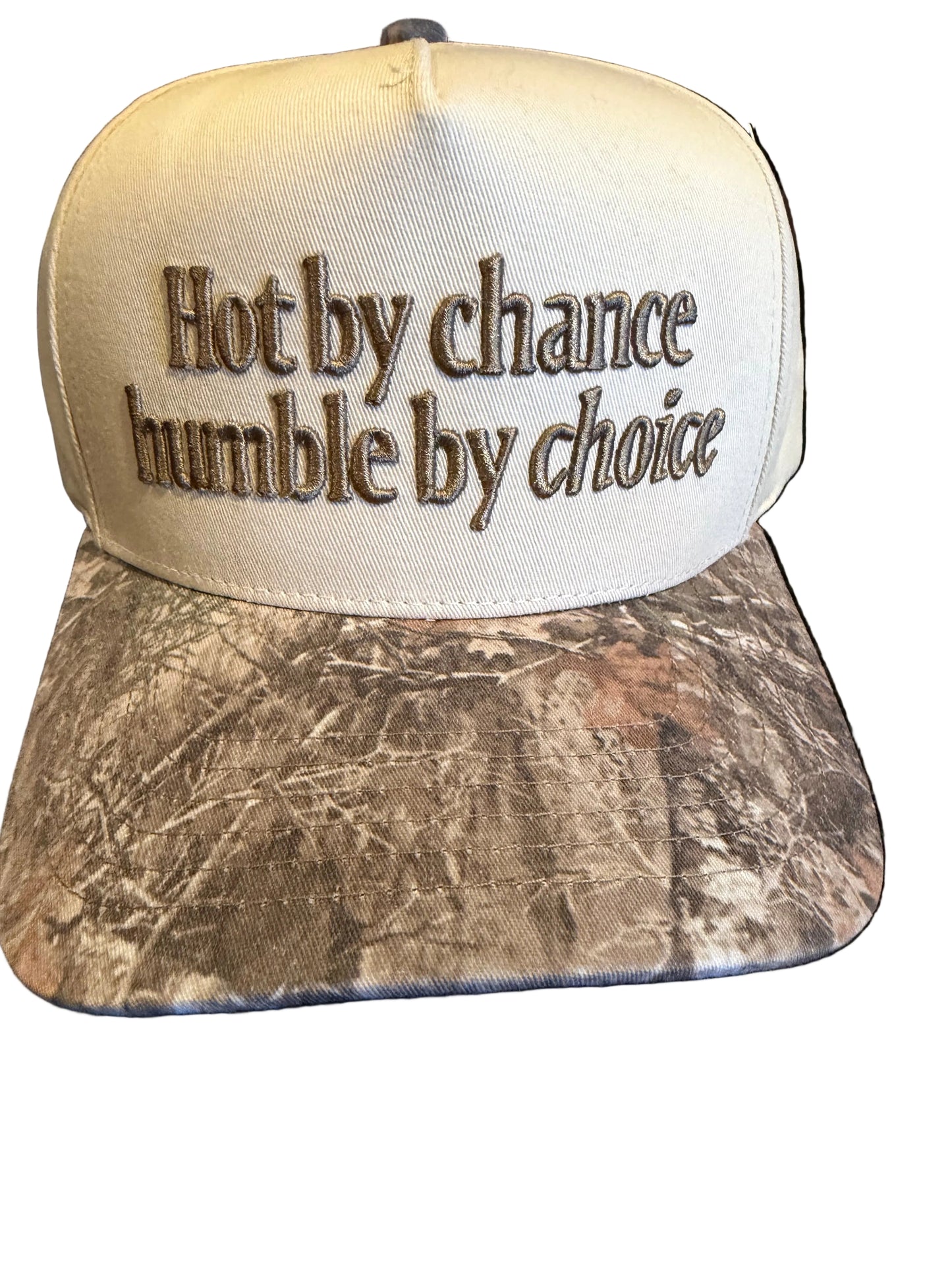 Cap with 'Hot by chance, humble by choice' text on a camouflage bill against a black background